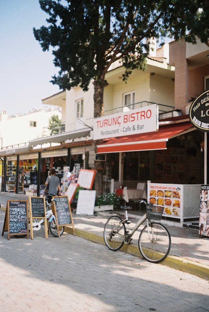 A lively city street scene featuring restaurants, shops, and bicycles on a sunny day.